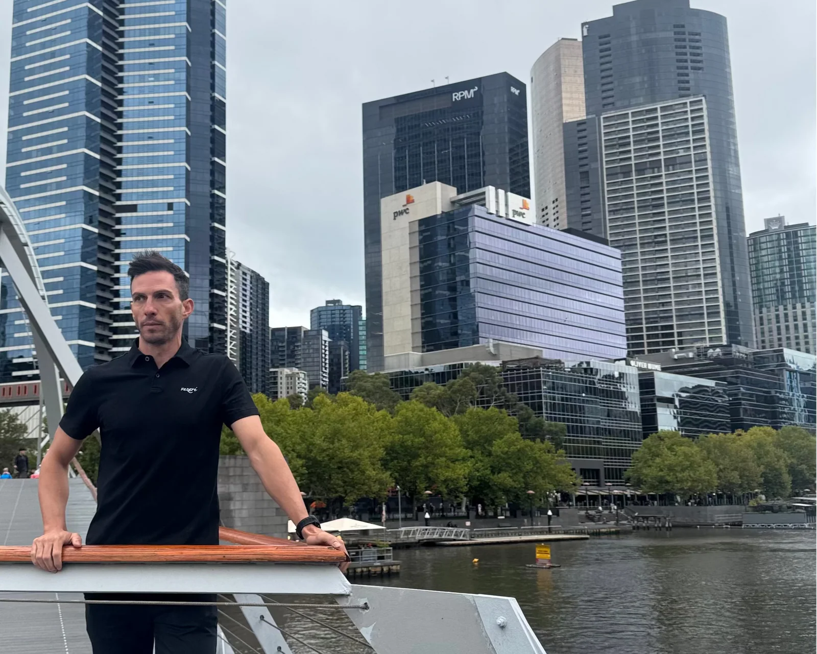 Man in the black vezari polo on a Southbank footbridge, Melbourne skyline behind